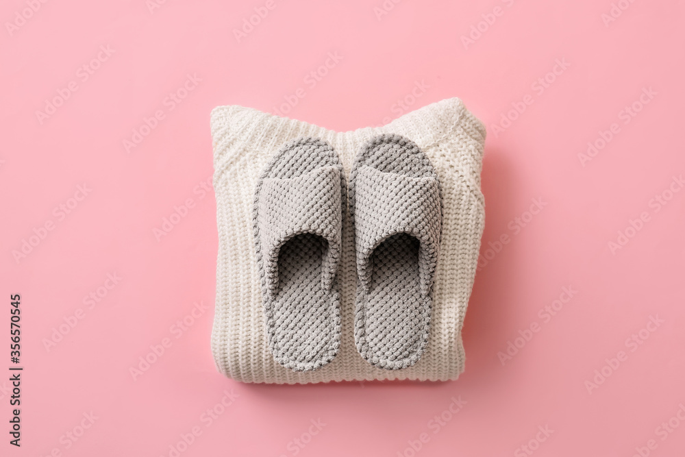 Pair of soft slippers and clothes on color background Pair of soft slippers and clothes on color background