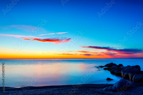 Vibrant colored spring sunset reflecting in ocean with endless horizon and deep blue ocean, silhouette of boulders laying in the foreground in shallow water at island of Gotland, Sweden © It4All