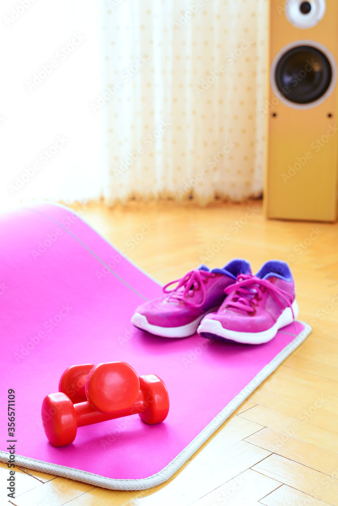 Low angle view of pink mat for workout, two red dumbbells and workout shoes - on wooden floor. Home training. Low angle view of pink mat for workout, two red dumbbells and workout shoes - on wooden floor. Home training.