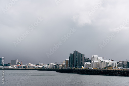 Multi-storey modern high-rise buildings on the waterfront in Reykjavik, the capital of Iceland. The shore of the Atlantic Ocean, the quiet water is calm. Cloudy sky, a blizzard is approaching. © Nadtochiy