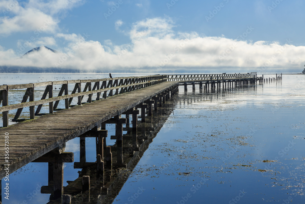 A long wooden wharf stretching far out into a lake. Historic Tokaanu Wharf on Lake Taupo, New Zealand
