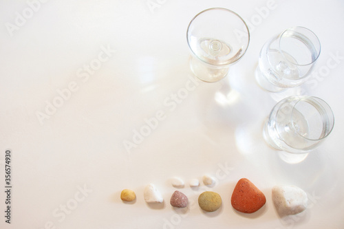 Three glasses of water  a heart shape and colorful stones on a white table. The heart shape created by light  shadow and glass of water.
