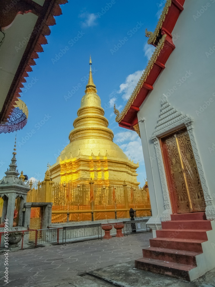 Naklejka premium view of Phra That Haripunchai, The Golden Pagoda (stupa, Chedi) with blue sky background, Wat Phra That Haripunchai Woramahawihan, Lamphun Province, northern of Thailand.