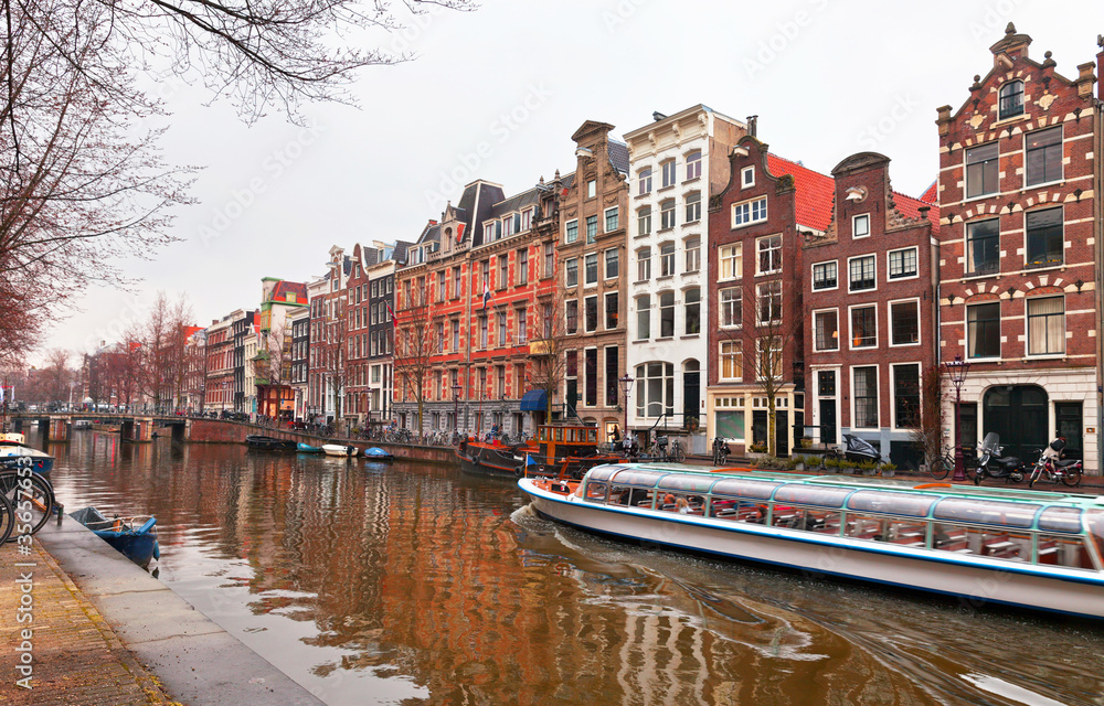 Naklejka premium Netherlands. Amsterdam. Tourists ride a pleasure boat along the Heerengracht canal and admire typical Dutch buildings with traditional pediments on spring day. Beautiful Holland cityscape