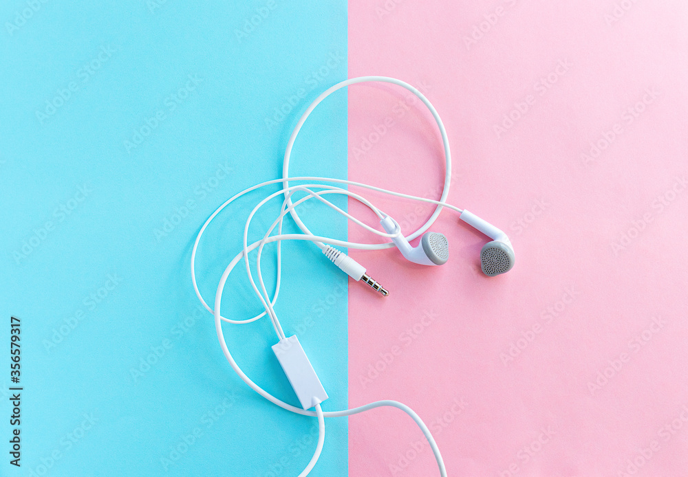 White wireless headphones on a pastel pink and blue background. The view from the top. copyspace White wireless headphones on a pastel pink and blue background. The view from the top. copyspace