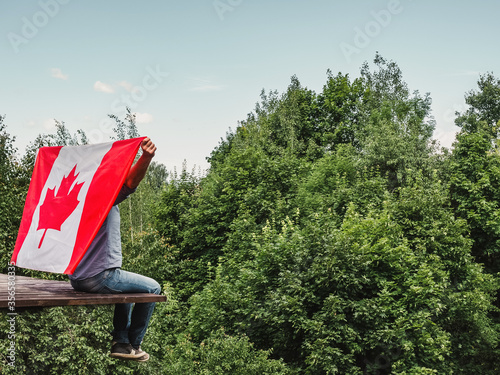 Attractive man holding Canadian Flag on blue sky background on a clear, sunny day. View from the back, close-up. National holiday concept photo