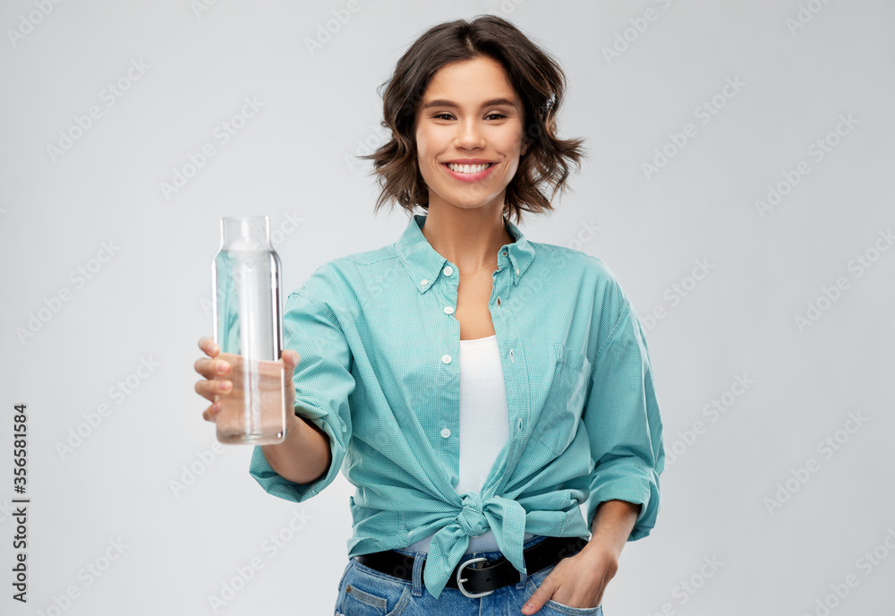 people concept - portrait of happy smiling young woman in turquoise shirt holding water in reusable glass bottle grey background people concept - portrait of happy smiling young woman in turquoise shirt holding water in reusable glass bottle grey background