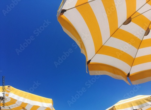 Low angle bottom view and detail of yellow and white beach or poolside umbrellas with a blue sky in the background - holiday and vacation concept