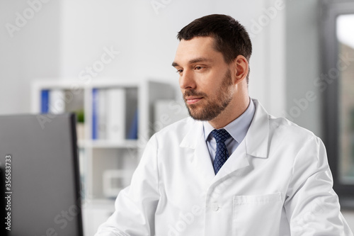healthcare  medicine and people concept - male doctor with computer working at hospital