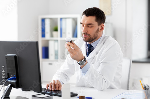 healthcare, medicine and people concept - male doctor with drug in jar and computer at hospital © Syda Productions