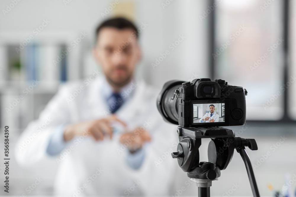healthcare, medicine and blogging concept - male doctor with camera and hand sanitizer recording video blog at hospital