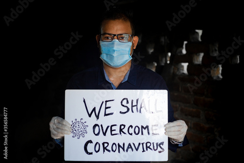 A young man wearing a medical mask and safety gloves stands with a placard message to 