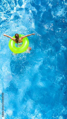 Active young girl in swimming pool aerial top view from above  child relaxes and swims on inflatable ring donut and has fun in water on family vacation  tropical holiday resort 