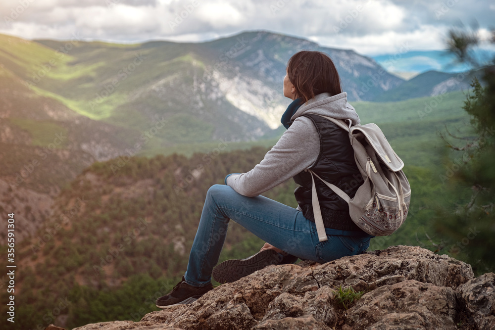 Young traveling woman on the top of the mountain cliff