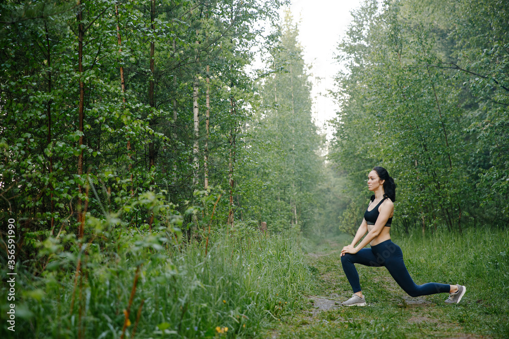 Athletic girl in leggings and top warming up in the woods
