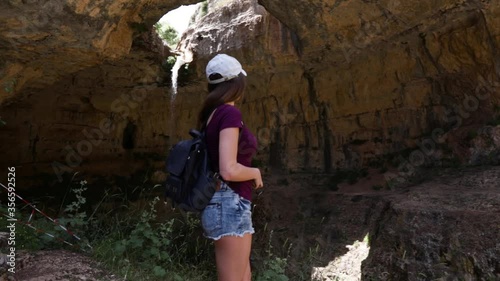 Young Caucasian Lebanese woman standing with phone and backpack looks up at Baatara gorge waterfall, Lebanon, close up slow motion pan photo