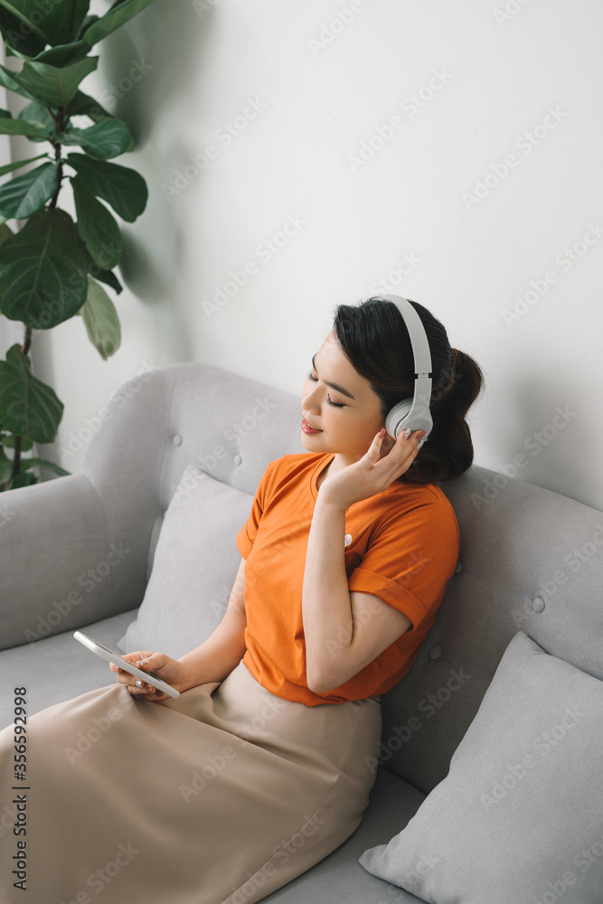Obraz premium Happy young woman with earphone dancing and listening to music on sofa