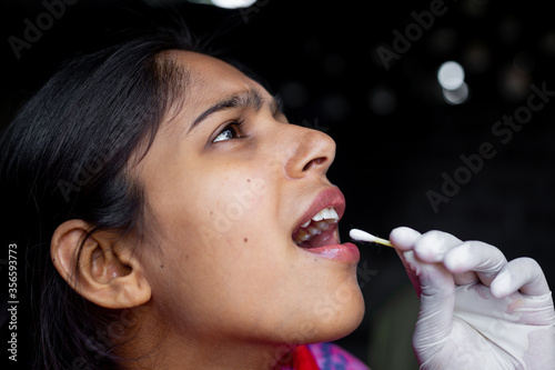 Doctor's hand taking Saliva test from young woman's mouth with Cotton Swab. Coronavirus Throat sample Collection. Close-up views.