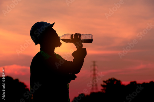 Silhouette engineer drinking fresh water when he feel thirsty after finish checking and inspection railway with twilight sky background.