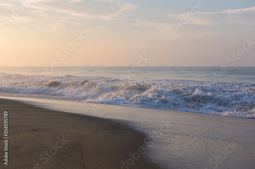 Beautiful seascape shot of the Indian ocean at sunrise with orange sand  a low tide with big white foamy waves and a blue orange sky on the horizon. Pitiwella beach  Sri Lanka