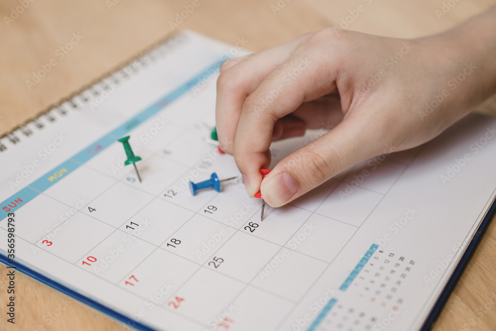 young woman's hand hold red push pin to marked on calendar young woman's hand hold red push pin to marked on calendar