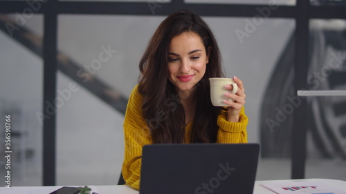 Closeup business woman looking laptop. Smiling girl drinking tea near notebook
