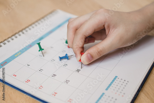 young woman's hand hold red push pin to marked on calendar