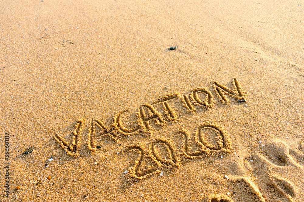 Fototapeta premium 2020 Vacation handwritten on sandy beach natural outdoors background.