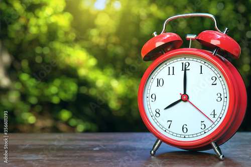 red alarm clock at 8 o'clock on wood with fresh green tree in background, happy morning time.