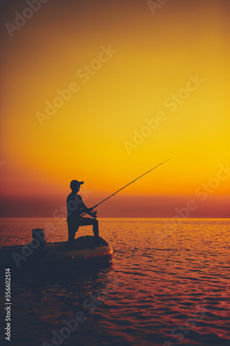 Silhouette of a fisherman fishing in sunset time on the open sea. © astrosystem
