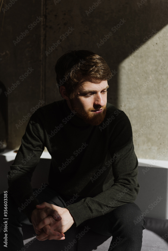 A young bearded man sits thoughtfully on the sofa.