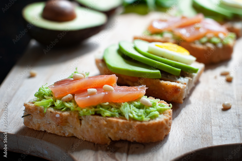 sandwiches with avocado, sliced egg, red fish and pine nuts on a wooden cutting board sandwiches with avocado, sliced egg, red fish and pine nuts on a wooden cutting board