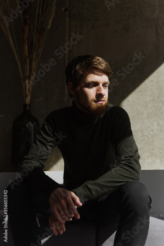 A young bearded man sits thoughtfully on the sofa. © Oksana