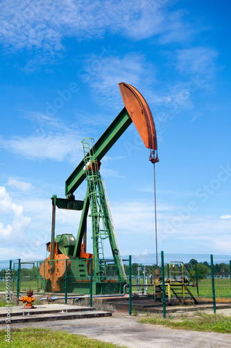 Oil pump jack in work. Oil industry in Seria, Brunei Darussalam on a sunny day with cloudy blue skies.