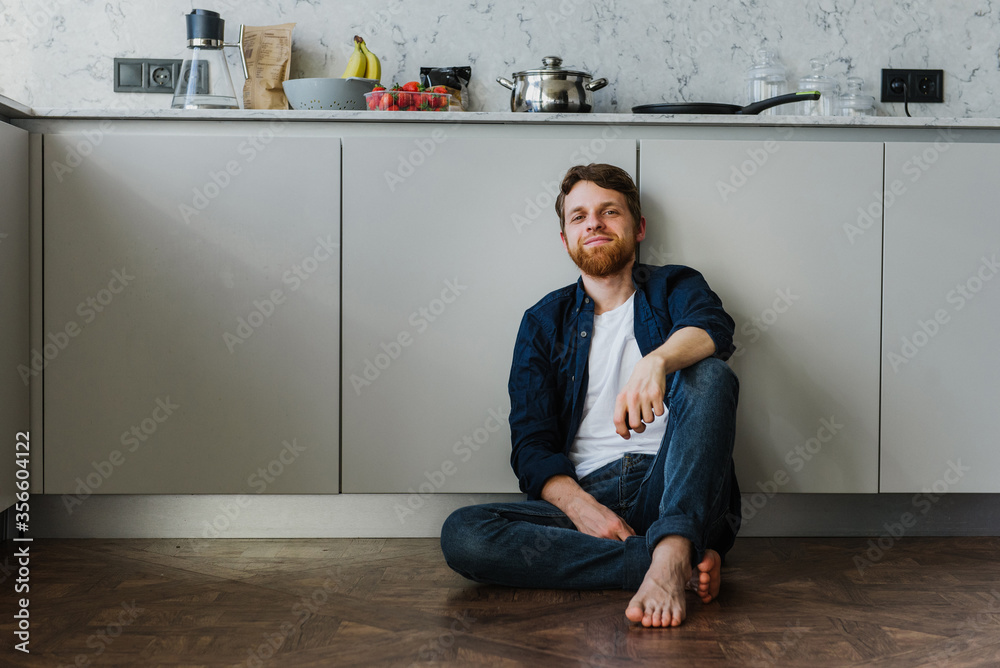 Young man smiling while sitting on the kitchen floor Young man smiling while sitting on the kitchen floor