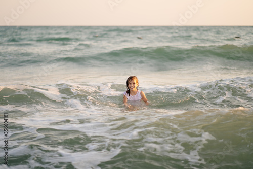teenager girl in dress swims in sea with high waves. entertainment in vacation. 