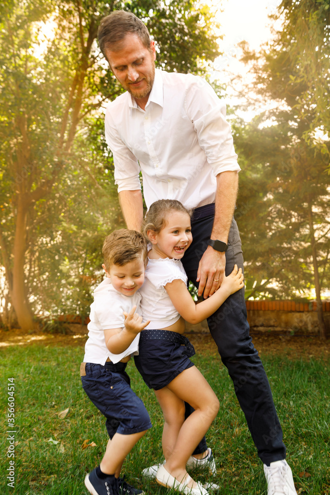 coppia di bellissimi bambini biondi gioca con il padre in giardino coppia di bellissimi bambini biondi gioca con il padre in giardino