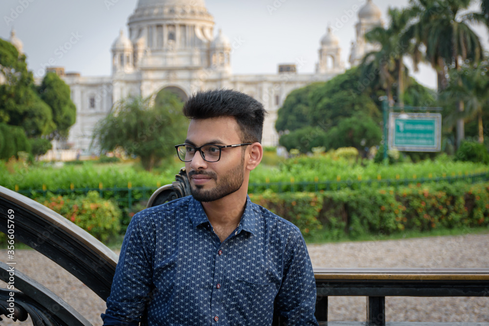 Portrait of a young and handsome Indian Bengali man standing in front of Victoria memorial wearing a blue shirt. Indian lifestyle and fashion Portrait of a young and handsome Indian Bengali man standing in front of Victoria memorial wearing a blue shirt. Indian lifestyle and fashion