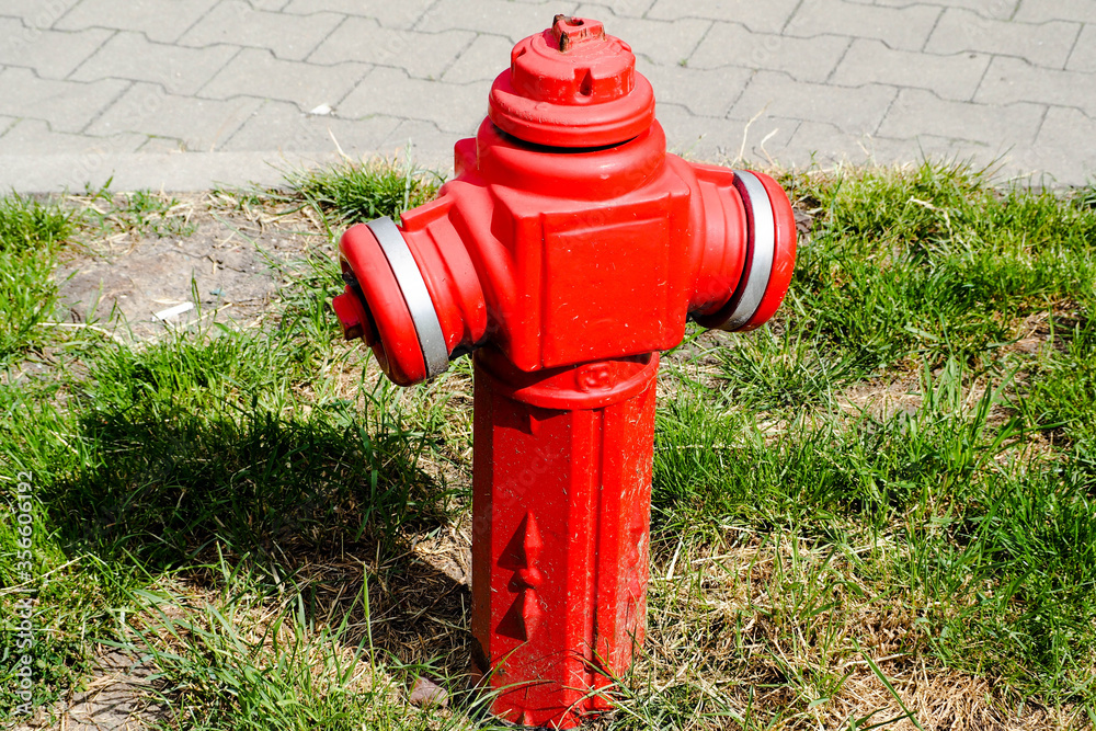 small old red and white fire hydrant on the background of the road and grass in the summer in the city of Europe
