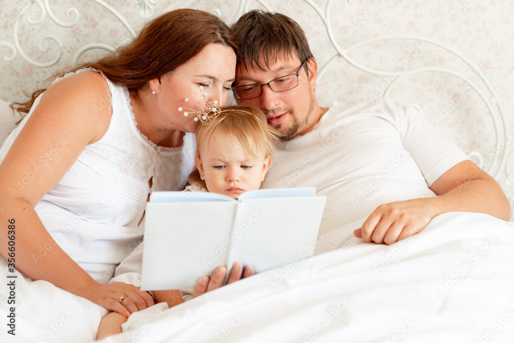 parents reading book to daughter in bed. place for text on white paper. parents reading book to daughter in bed. place for text on white paper.