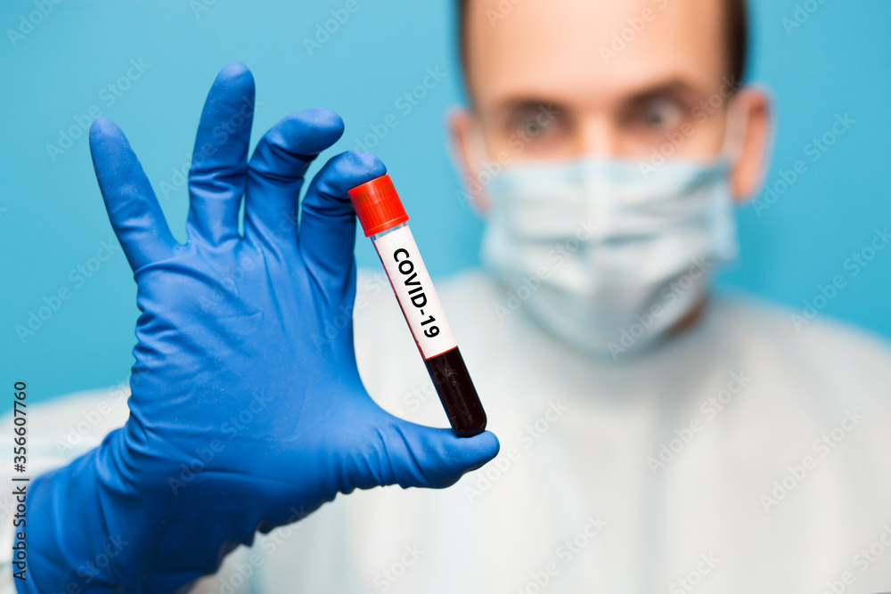 Doctor in protective mask and gloves holds test tube containing blood sample that has tested for coronavirus. Laboratory testing patients blood for presence of coronavirus COVID-19. Doctor in protective mask and gloves holds test tube containing blood sample that has tested for coronavirus. Laboratory testing patients blood for presence of coronavirus COVID-19.