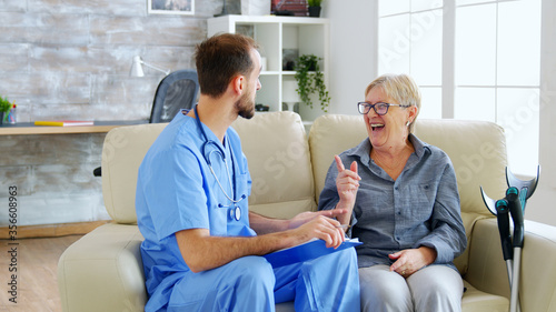 Doctor assistant taking notes on clipboard while listening to old retired woman in nursing home. Caregiver and social worker