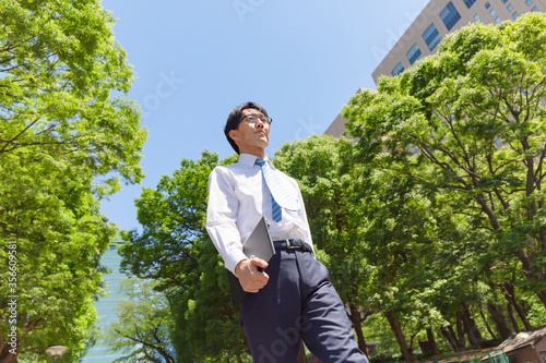 やせ型の真面目そうな日本人ビジネスマンがパソコンを持って歩いている