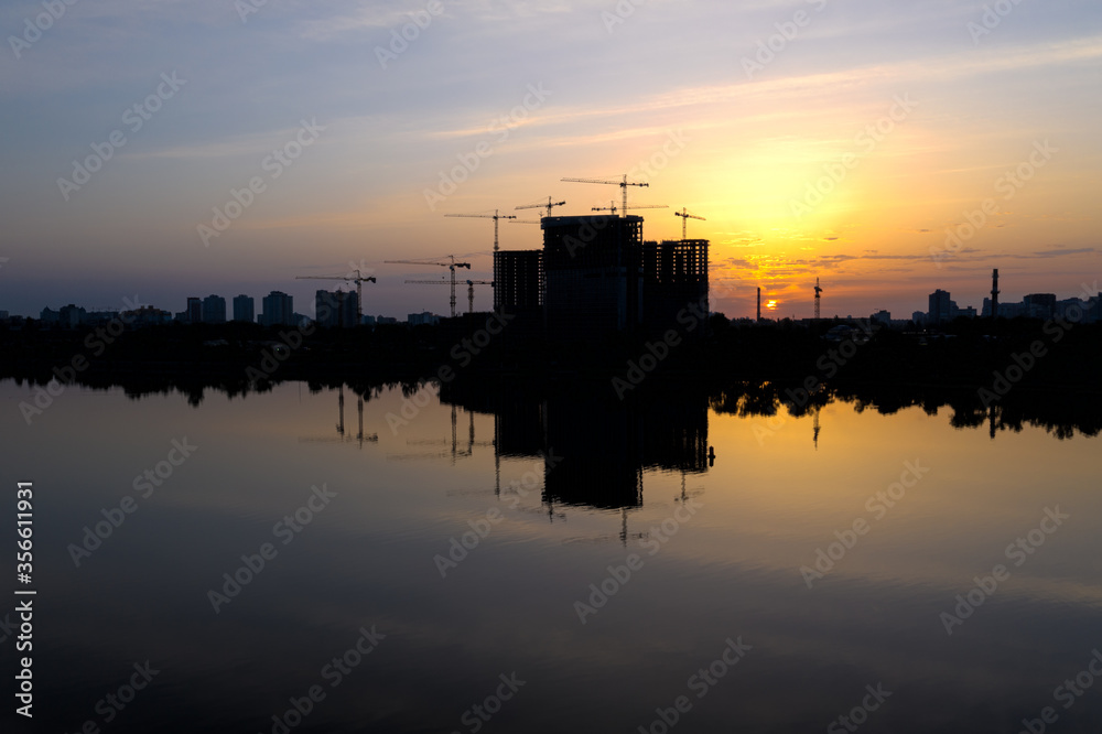 Beautiful urban construction site silhouettes at Dawn. Morning Cityscape with Reflection in water.