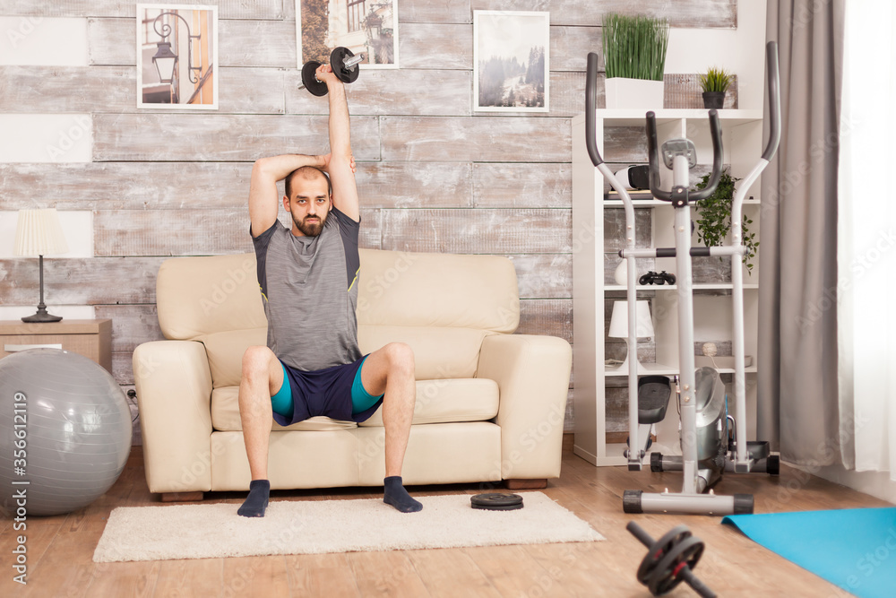 Athletic man increase his triceps strength using dumbbell during global self isolation. Athletic man increase his triceps strength using dumbbell during global self isolation.