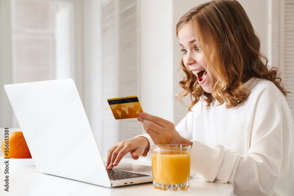 Photo of excited cute girl using laptop and holding credit card