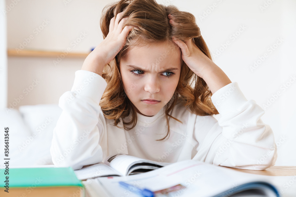 Photo of caucasian furious girl grabbing her head while doing homework Photo of caucasian furious girl grabbing her head while doing homework