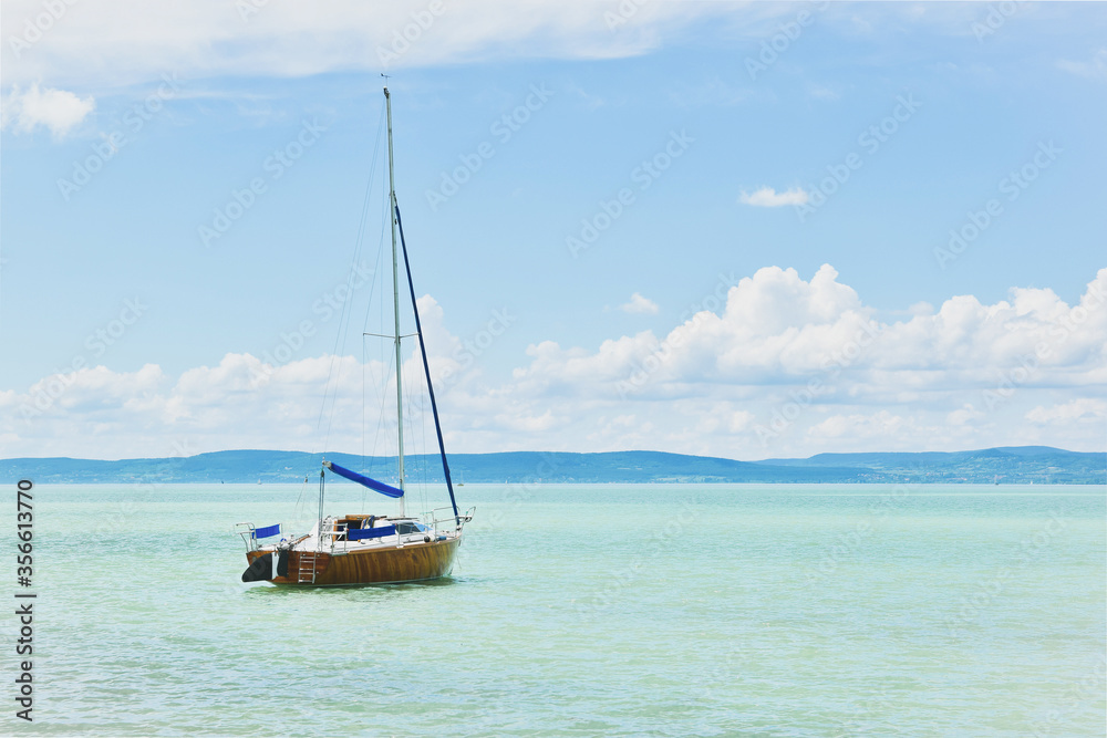 Sailboat floating peacefully on the azurre blue water of Lake Balaton, clear blue water with a sailing boat daylight view,summer water sport, Lake Balaton, Hungary landscape, vacation on the beach Sailboat floating peacefully on the azurre blue water of Lake Balaton, clear blue water with a sailing boat daylight view,summer water sport, Lake Balaton, Hungary landscape, vacation on the beach