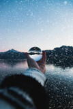 man holding a glassball in front of snowy background with mountains and a lake. Snowing