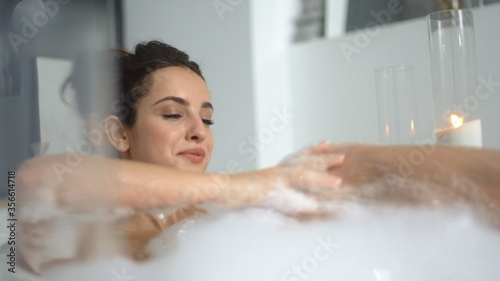 Close up hot woman lying in foam at bathroom. Sexy girl relaxing at luxury bath.